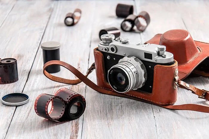film camera in a brown leather case surrounded by film rolls
